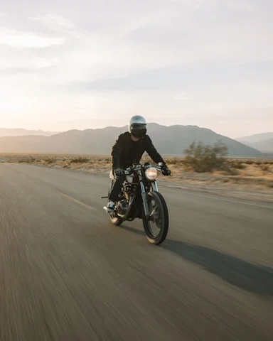 Person wearing a helmet riding a motorcycle on an open road with mountains in the background during sunset.