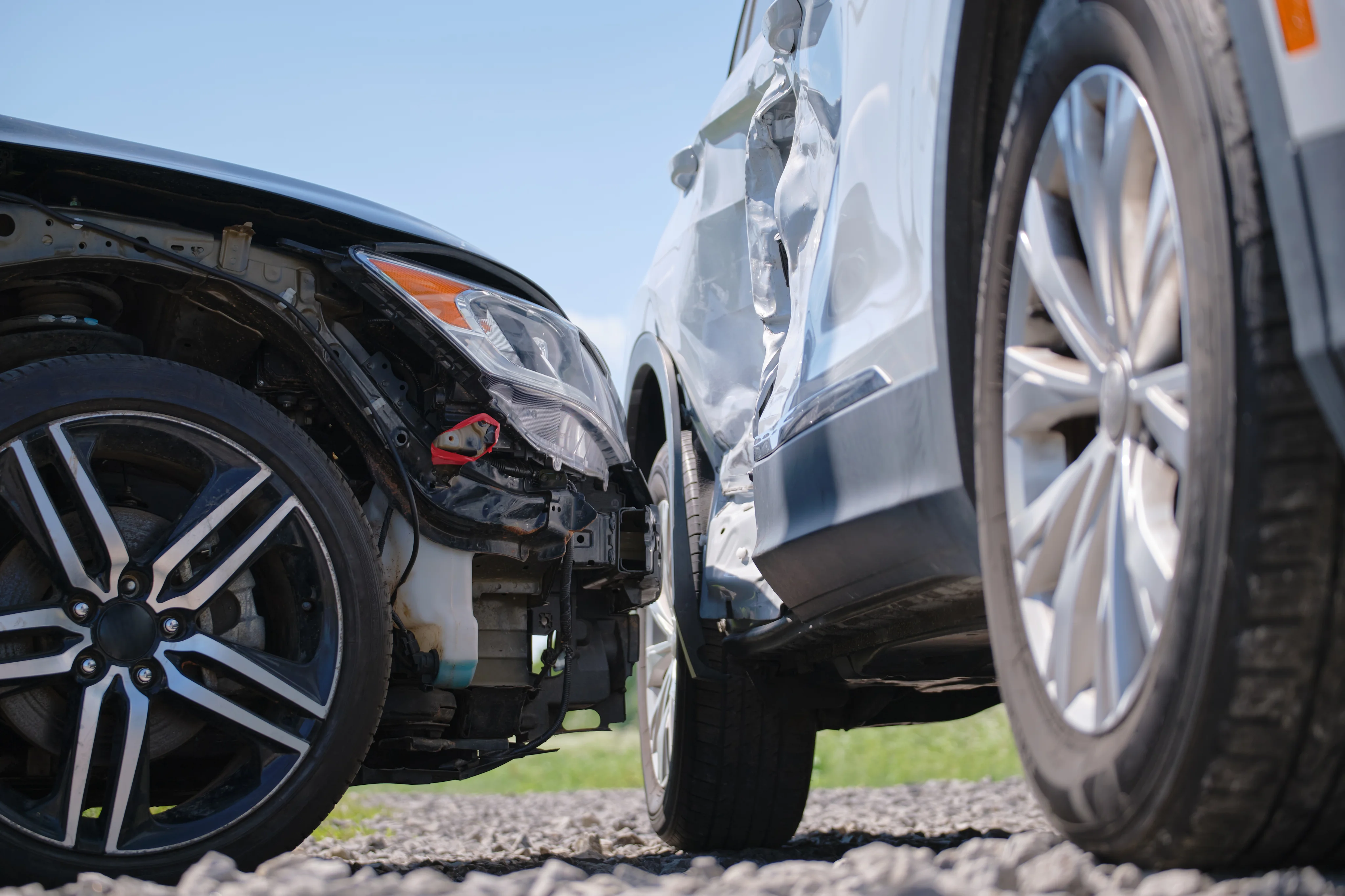 Close-up of two cars involved in a collision, showing damage to the front of one car and the side of the other on a gravel surface.