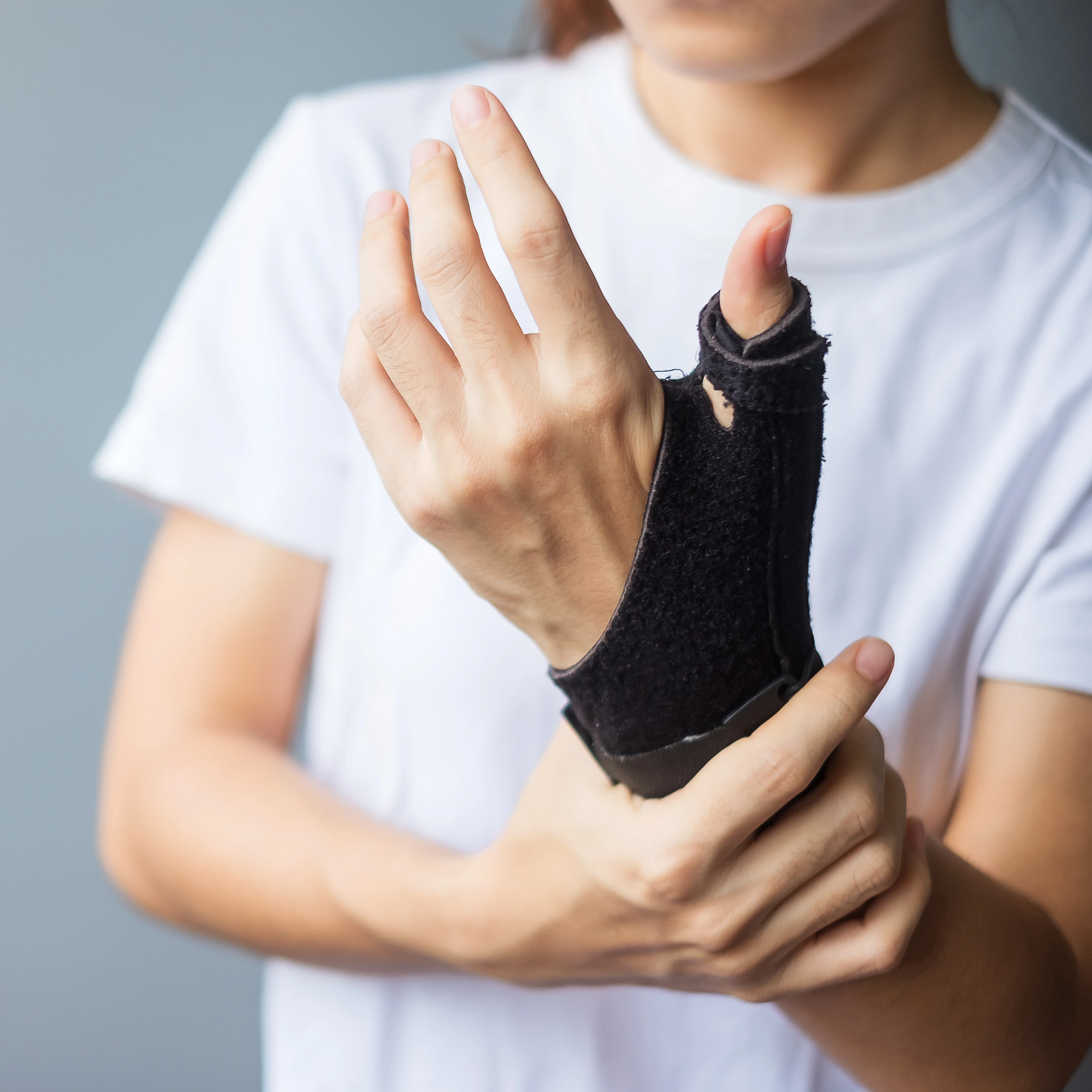 Person adjusting a black wrist brace on their left hand, wearing a white shirt.