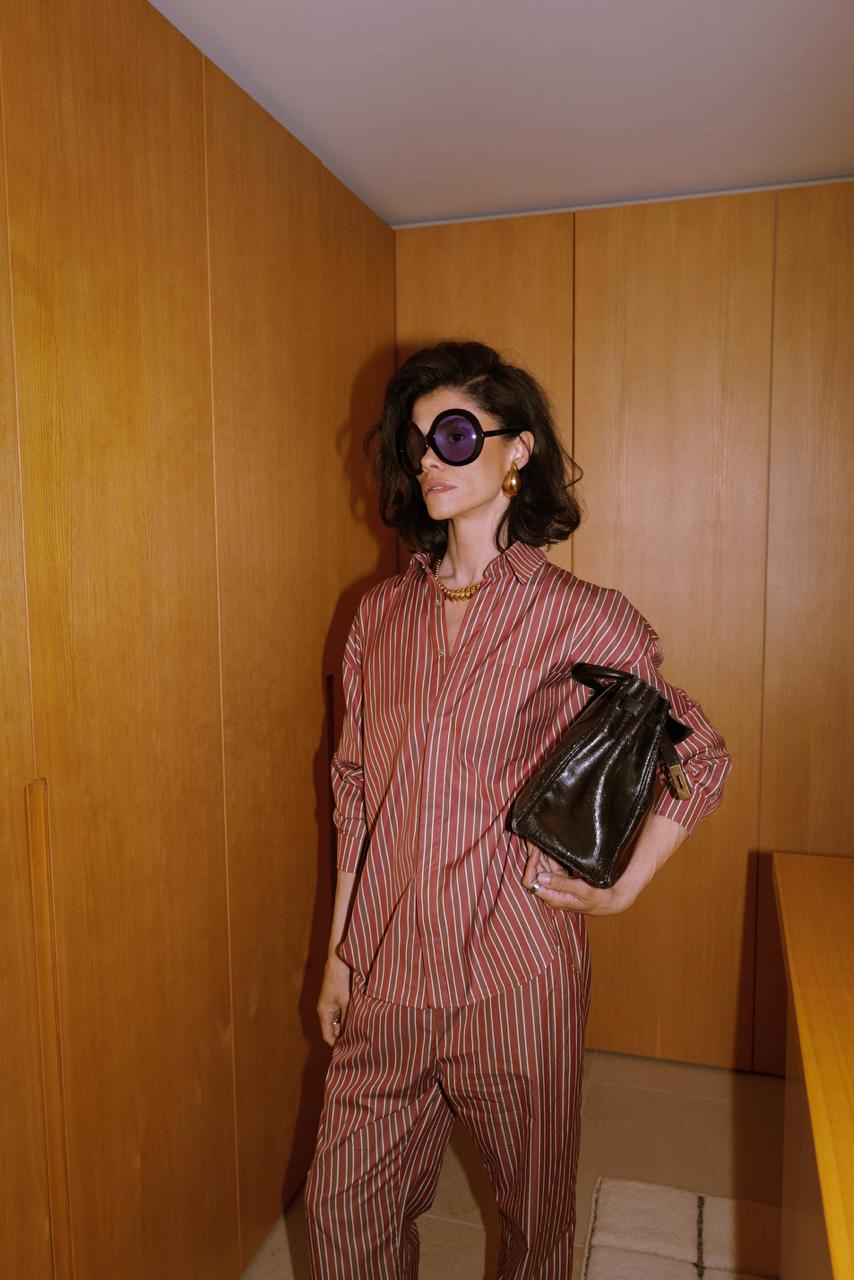 Woman standing full length in a brown cotton pajama set by a bedroom window