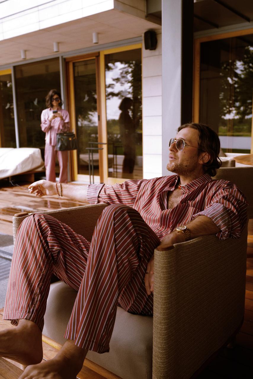 Man and woman in striped summer sets on a terrace beside a modern lake house