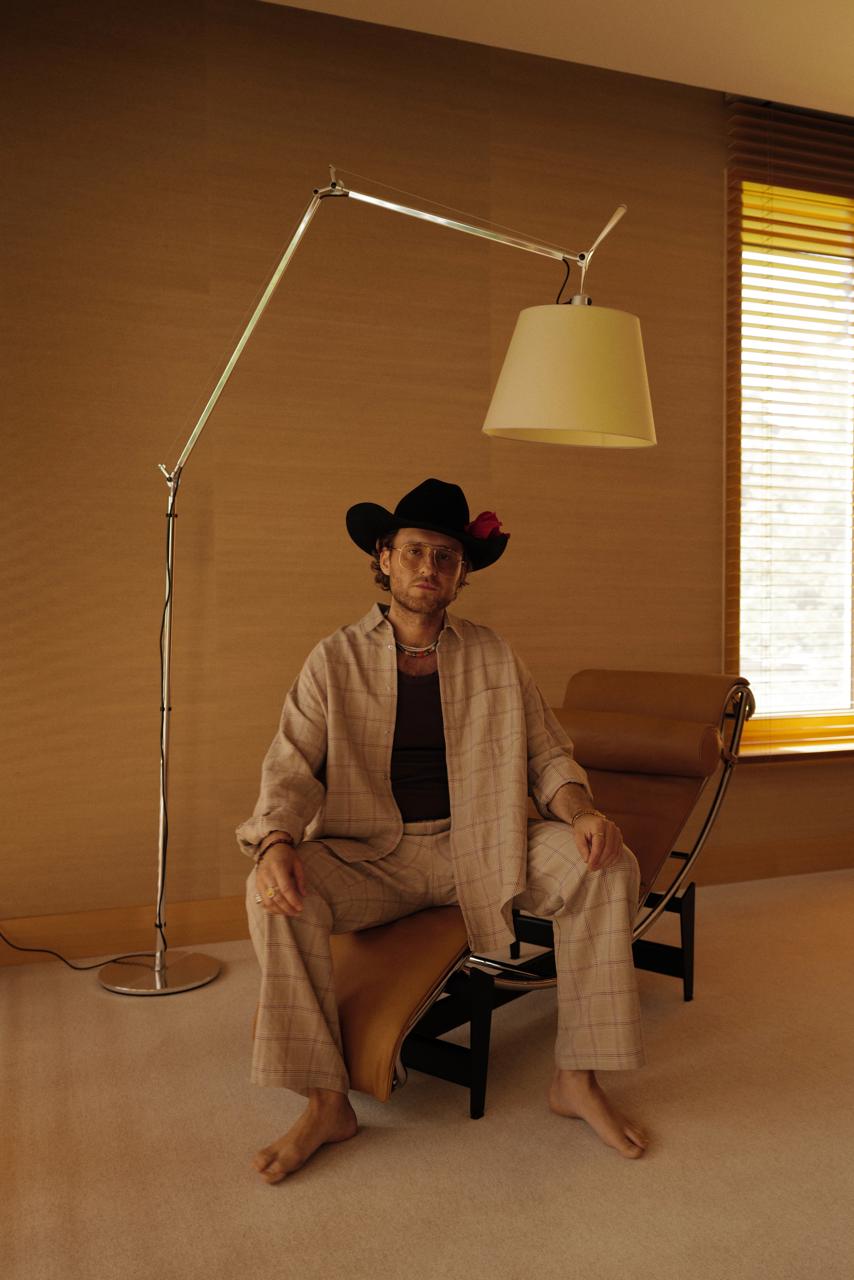 Woman in a striped cotton pajama set sitting on a daybed, sunglasses on, a polka-dot tie loose at the neck