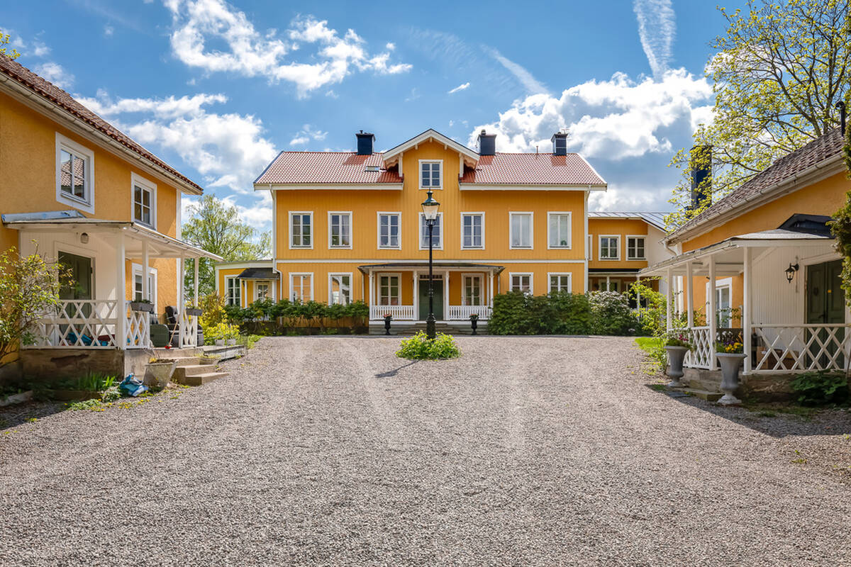 Gul herrgårdsbyggnad på Eriksberg utanför Norrköping, sedd från gårdsplanen med två mindre sidobyggnader och nyrenoverat tak i tegel.