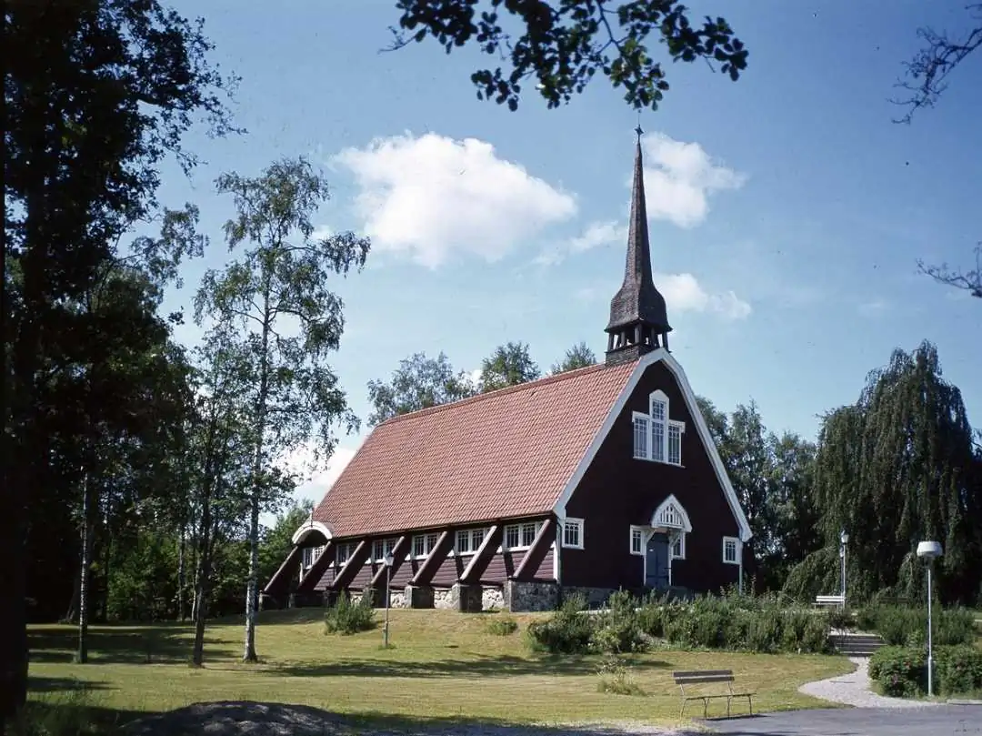 Träkyrka i Hindås omgiven av grön park och höga träd.
