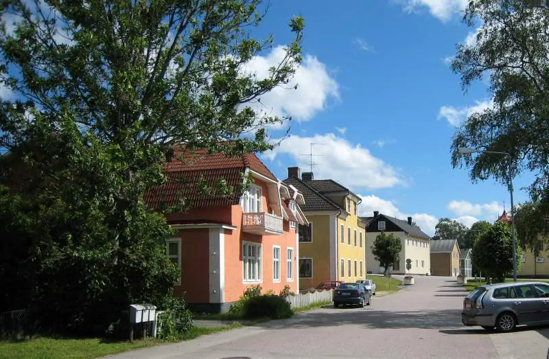 Gatumiljö i Åseda med trähus, trottoar och grönskande träd.