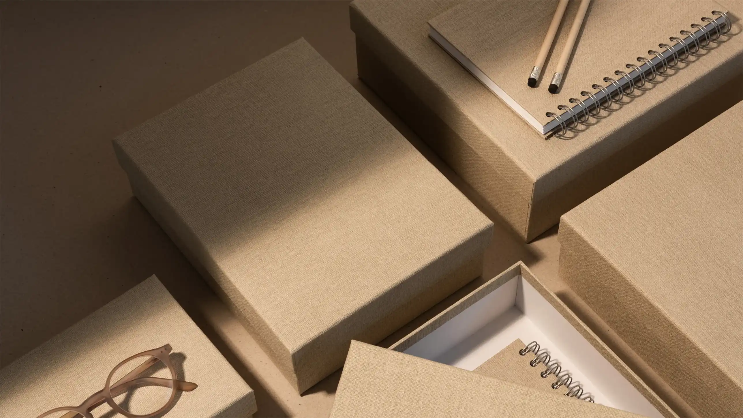 Bigso beige fabric-covered storage boxes arranged on a desk with a spiral notebook, pencils, and eyeglasses, offering stylish and practical home office organization.