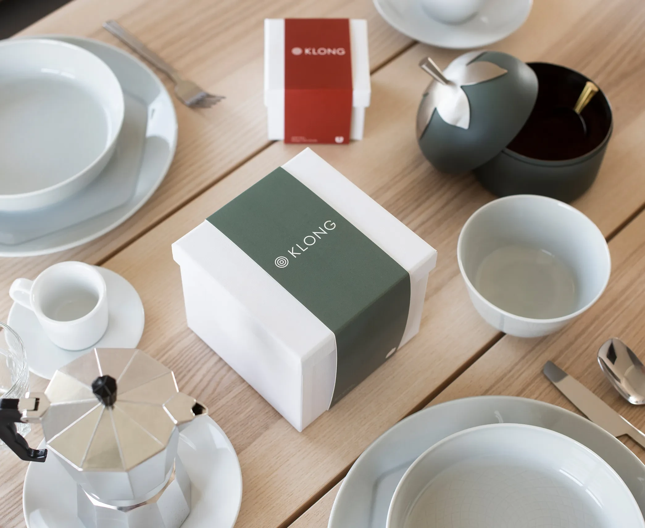 KLONG-branded white gift box with green sleeve placed on a breakfast table set with cups, plates, coffee maker, and modern tableware.