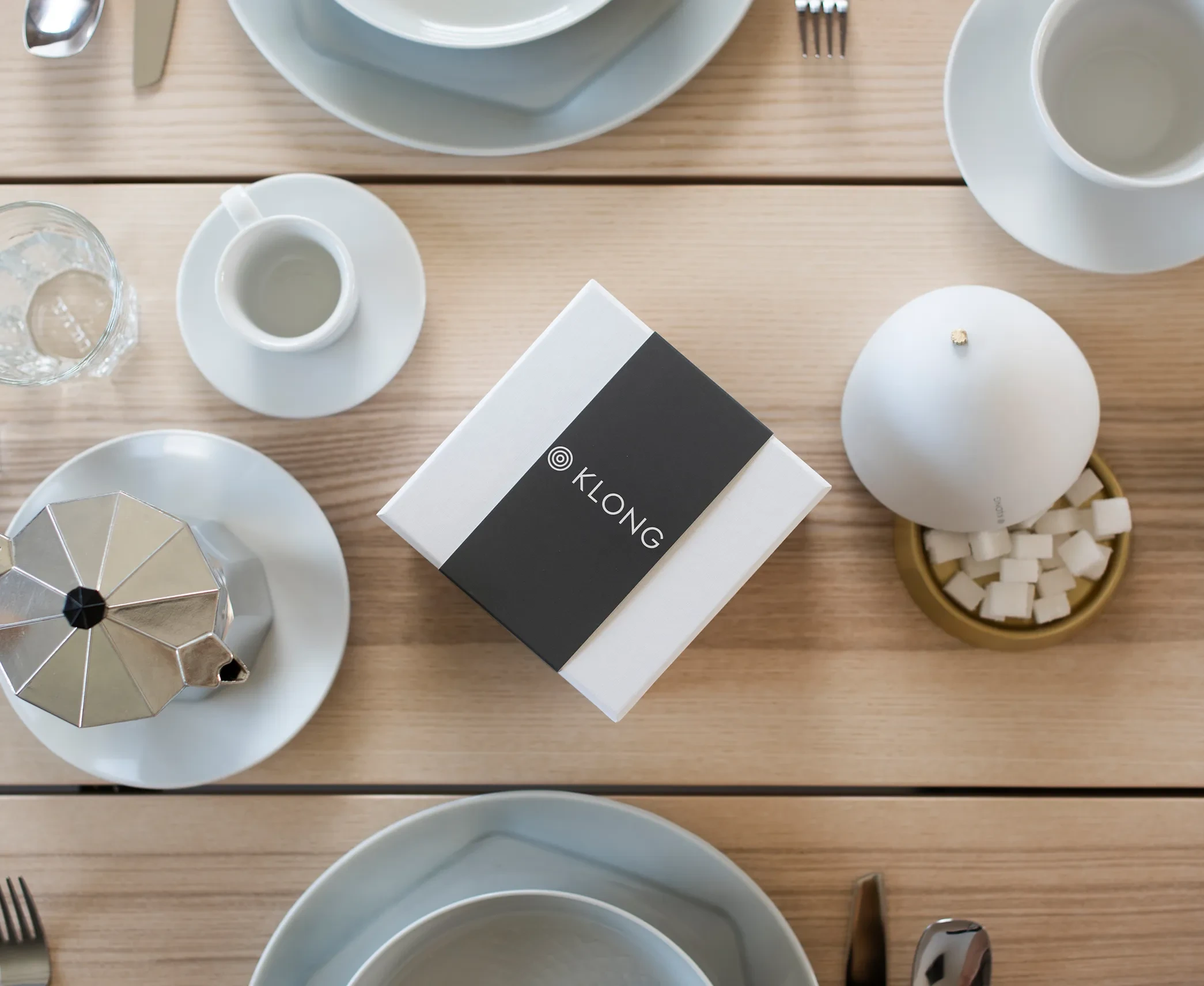 KLONG-branded white gift box with black sleeve placed on a neatly set breakfast table with coffee, sugar bowl, and modern tableware.