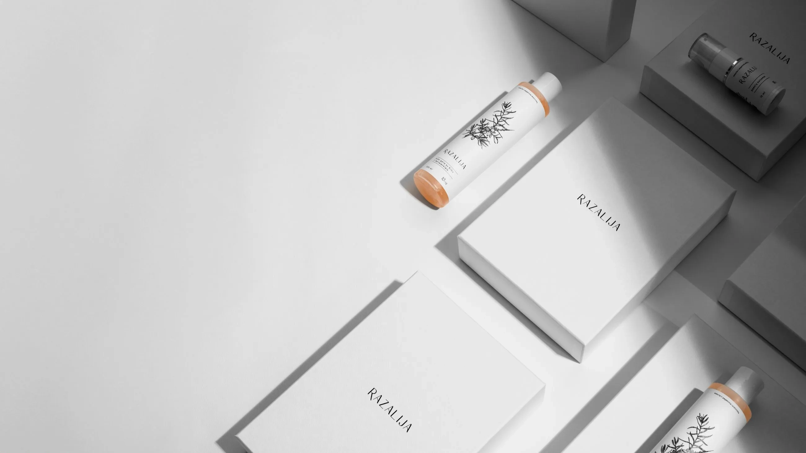 Minimalist luxury packaging for Razalija skincare products, featuring white rigid boxes and elegant botanical-illustrated bottles, designed by Bigso.