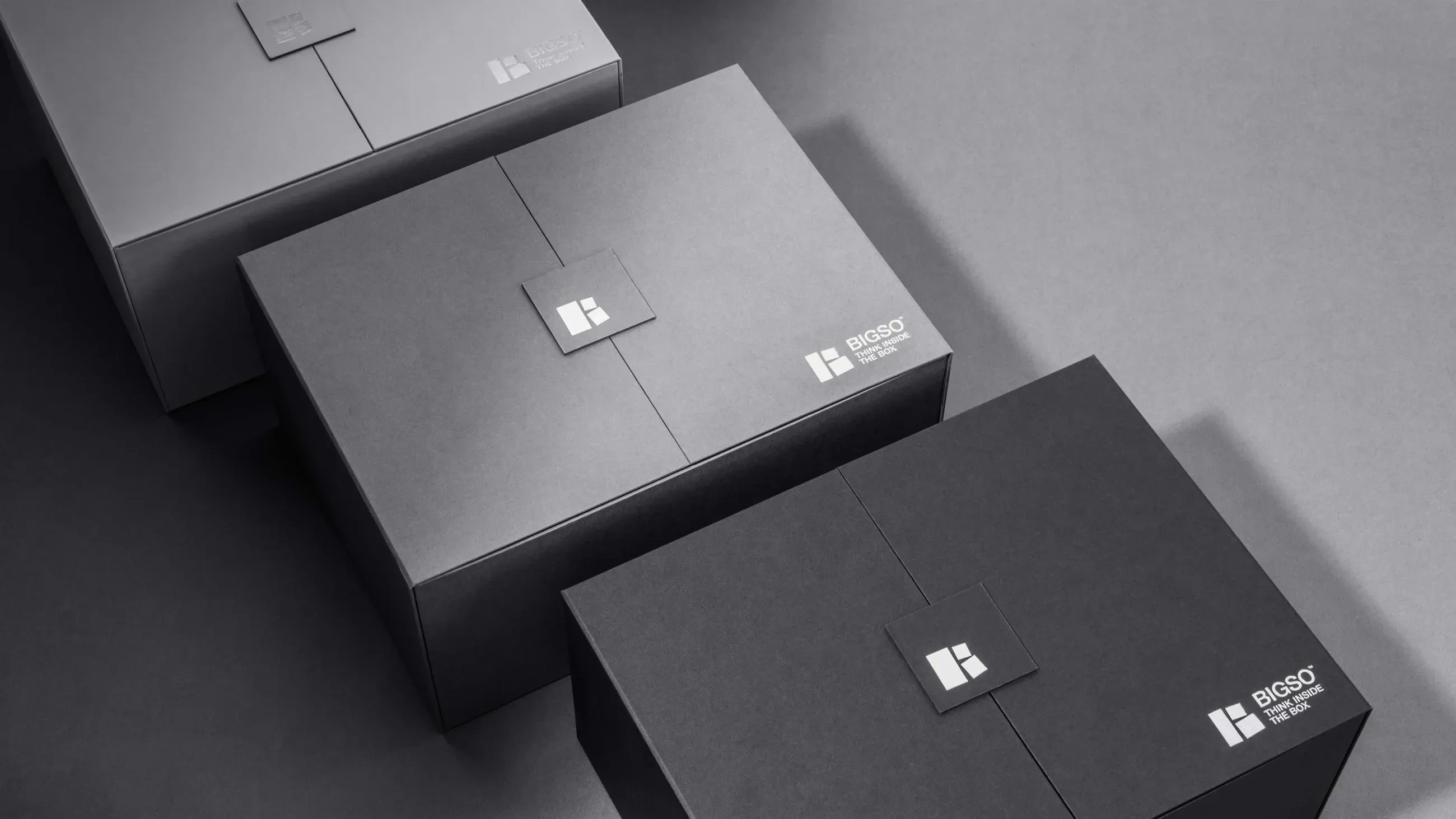 Premium black and grey Bigso storage boxes with sleek minimalist design and logo branding, arranged in a flat lay on a dark background, showcasing modern high-quality packaging solutions.