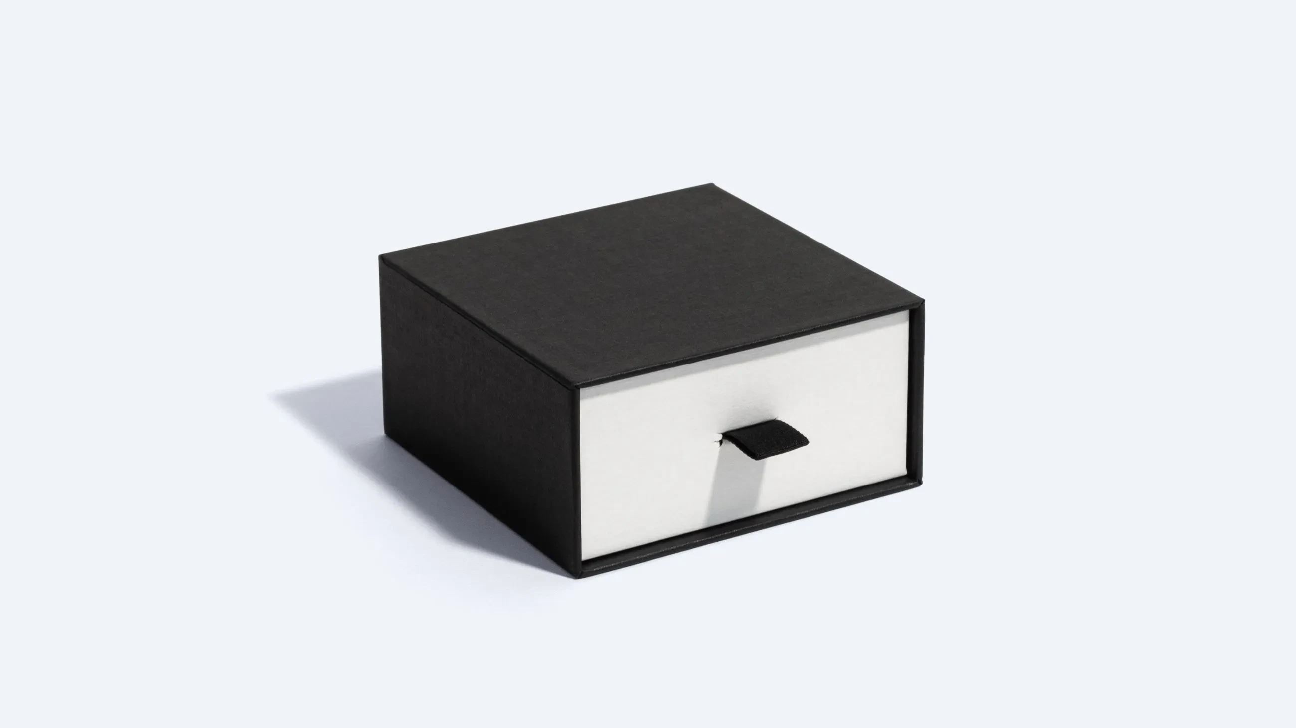 A black and white rigid drawer box with a small pull-tab for sliding the inner compartment.