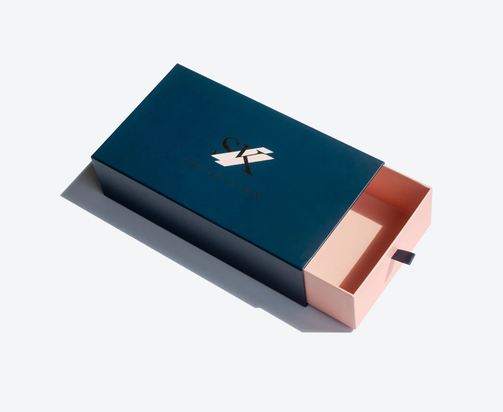 A two-tone rigid drawer box in navy blue and blush pink, featuring a black pull-tab on the tray.