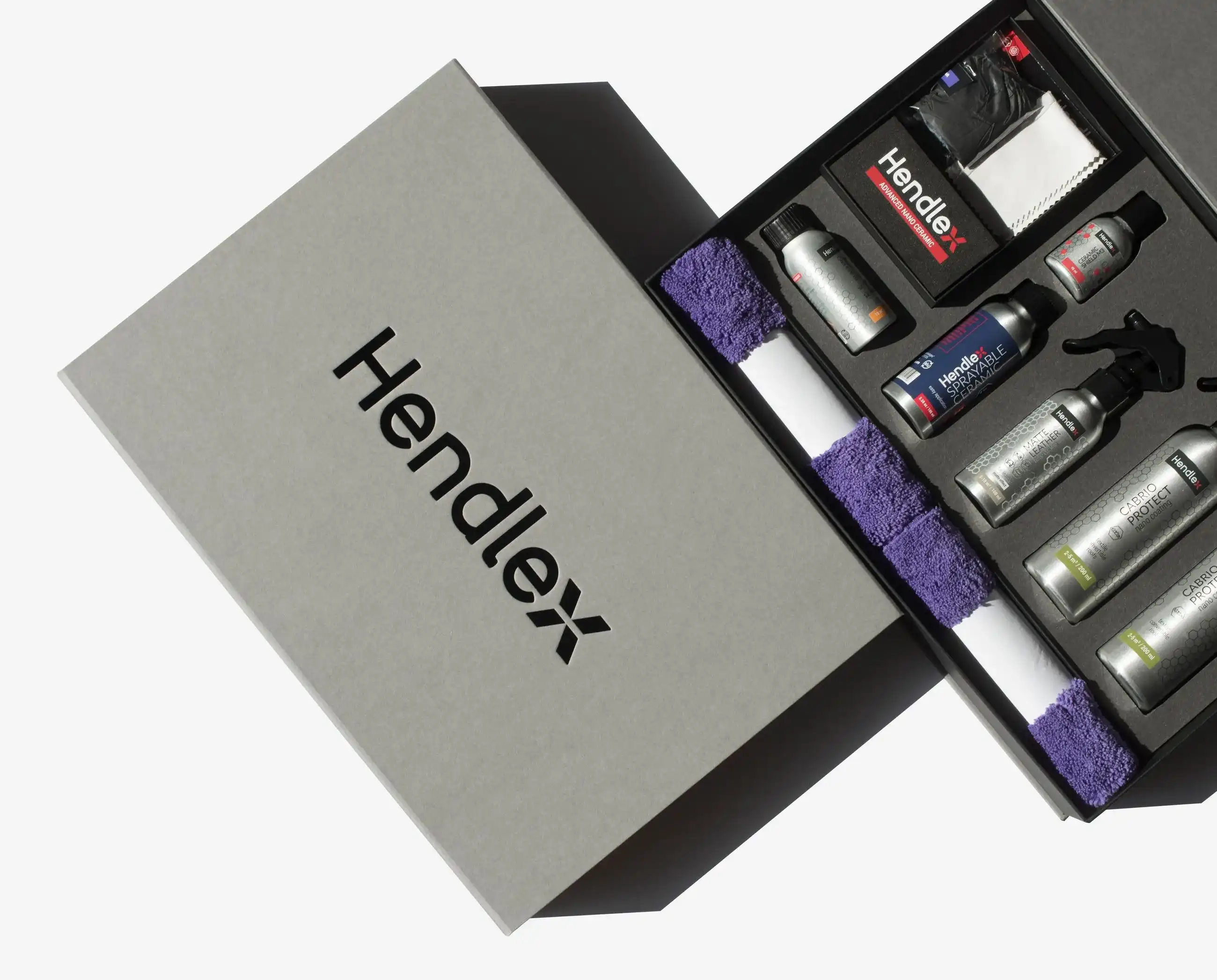 A grey magnetic box with the Hendlex logo, shown partially open to reveal neatly arranged product bottles and accessories inside.