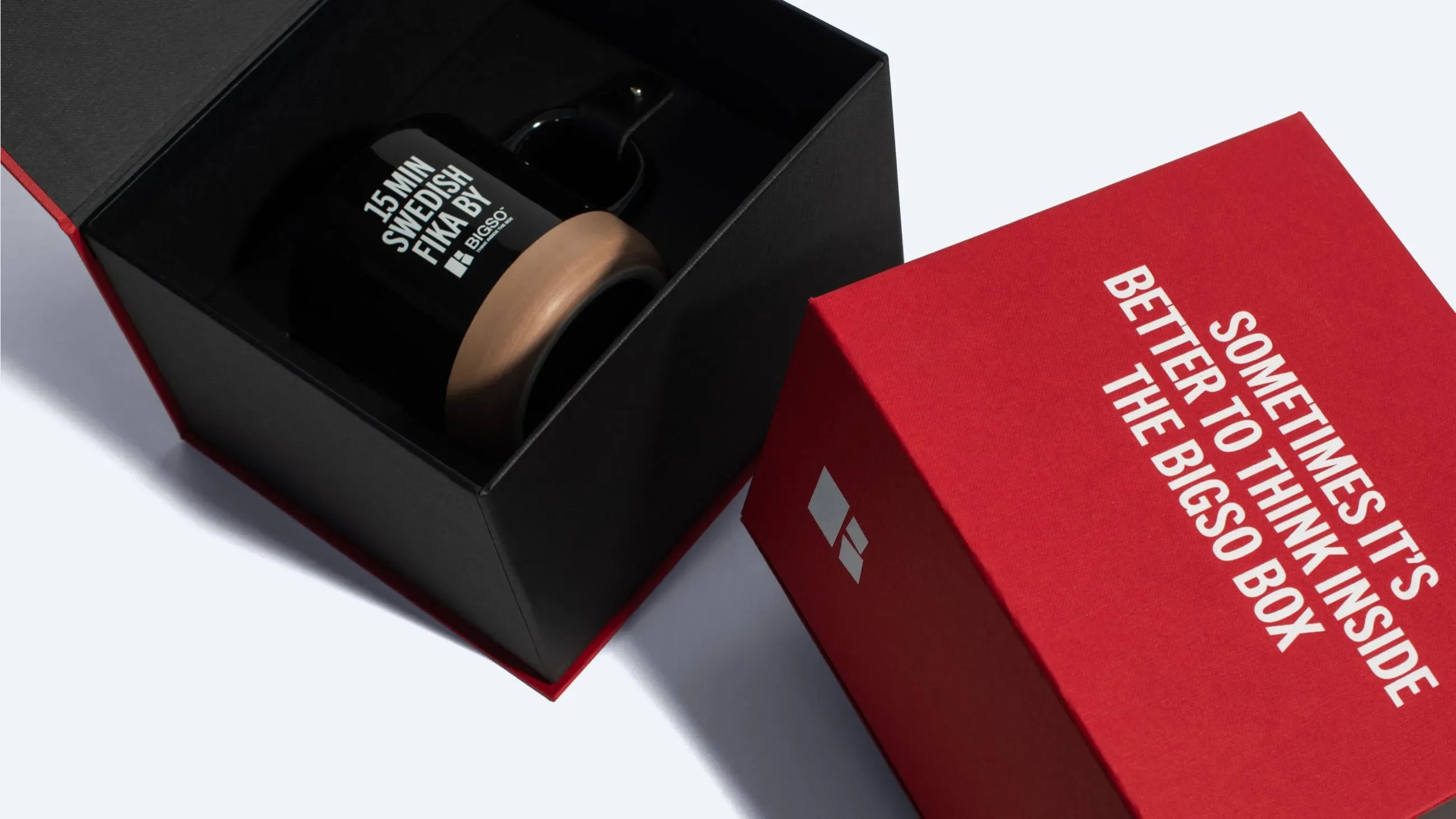 A red and black magnetic box with the lid removed, holding a branded black mug inside.