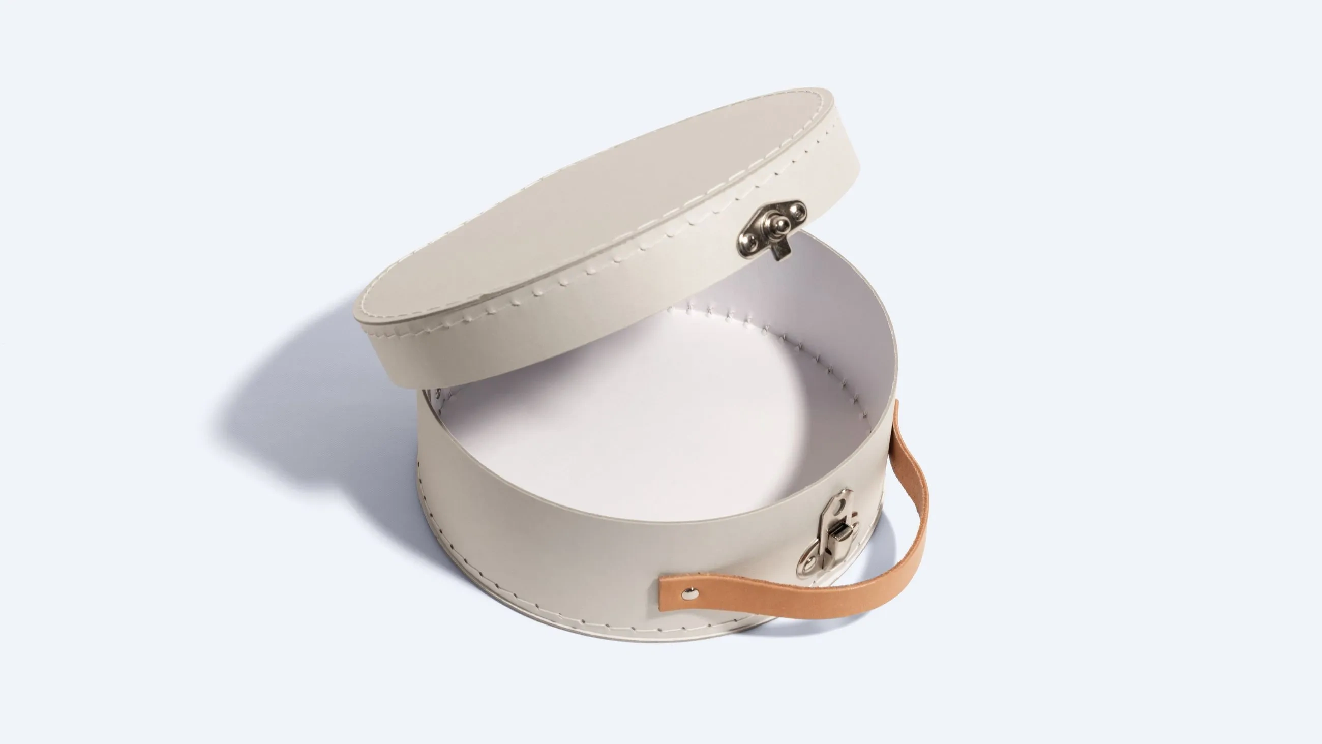 Rigid round suitcase box with leather handle and metal clasp, made from stitched riveted cardboard.