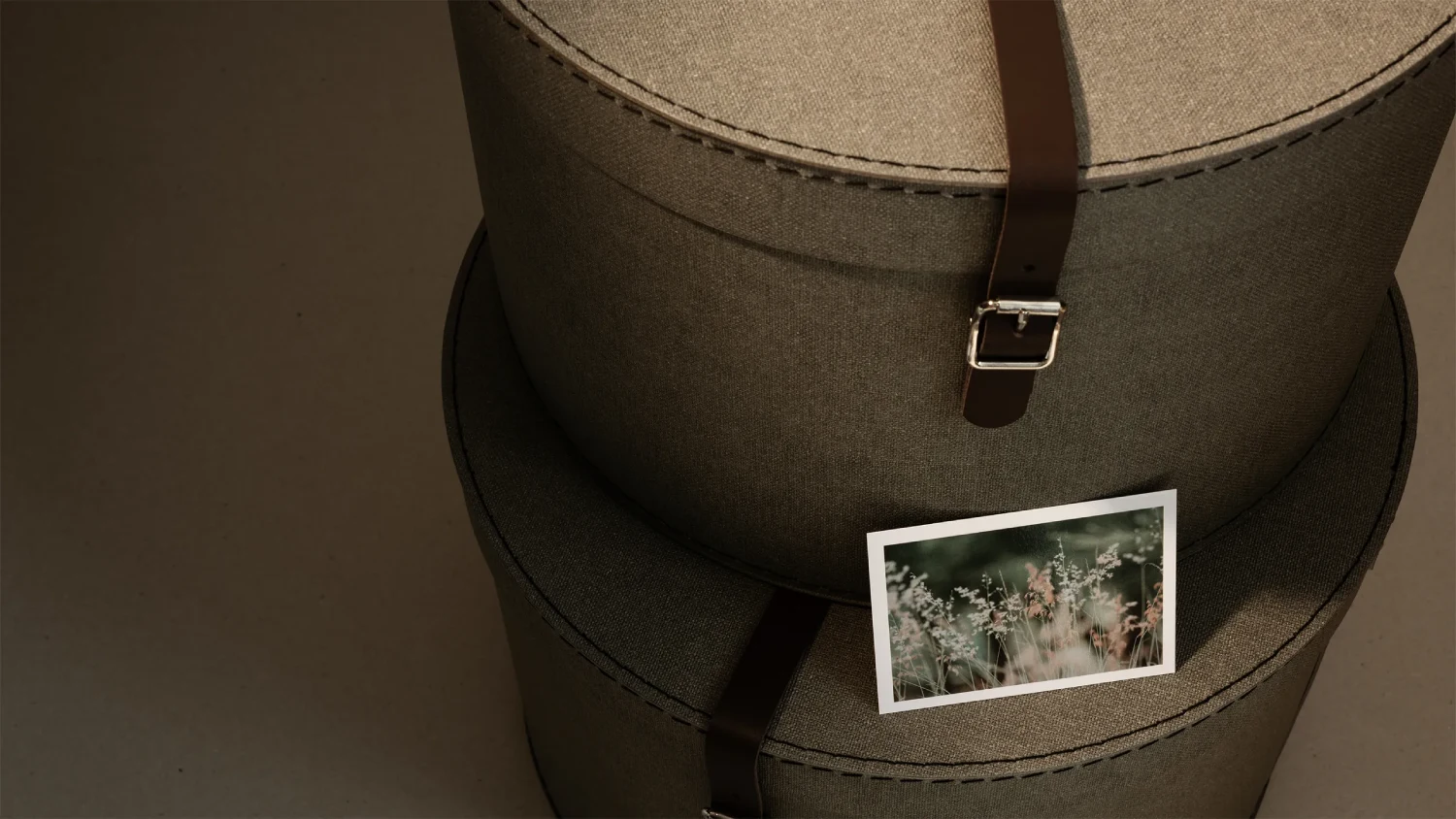Stack of round fabric-covered storage boxes in earthy tones with leather strap closures and visible stitched details, highlighting Bigso’s premium sustainable materials and timeless Scandinavian design. A postcard rests on the box, emphasizing natural inspiration in eco-friendly packaging and home organization solutions.