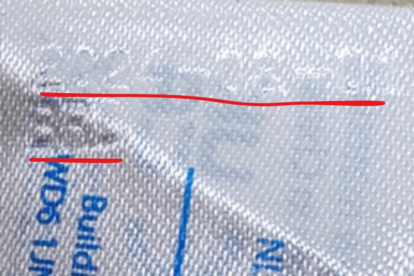 Lähikuva leikkimaton pesuohjelapusta, jossa näkyy lappuun kohopainettu eränumero. Eränumero on kuvan päälle alleviivattu punaisella viivalla.