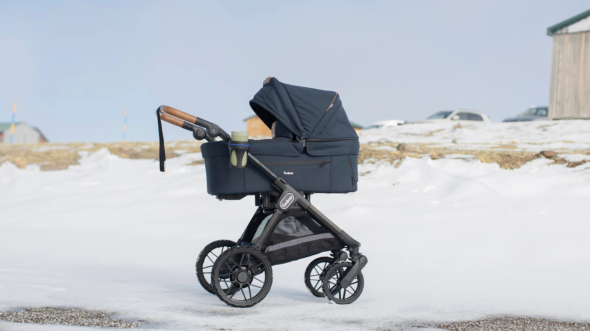 A stylish Emmaljunga stroller parked on a scenic winter scene with a snowy background.
