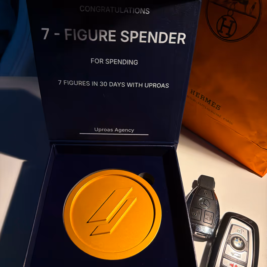 Black box with a gold-colored medallion inside and text congratulating a 7-figure spender for spending 7 figures in 30 days with Uproas, alongside Mercedes and BMW car keys and an orange Hermes bag.