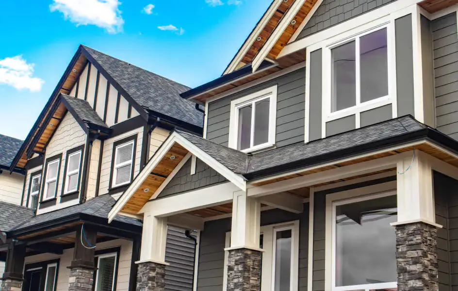 Two-story home exterior with gray siding, white trim, stone accents, and wood-paneled gable roof