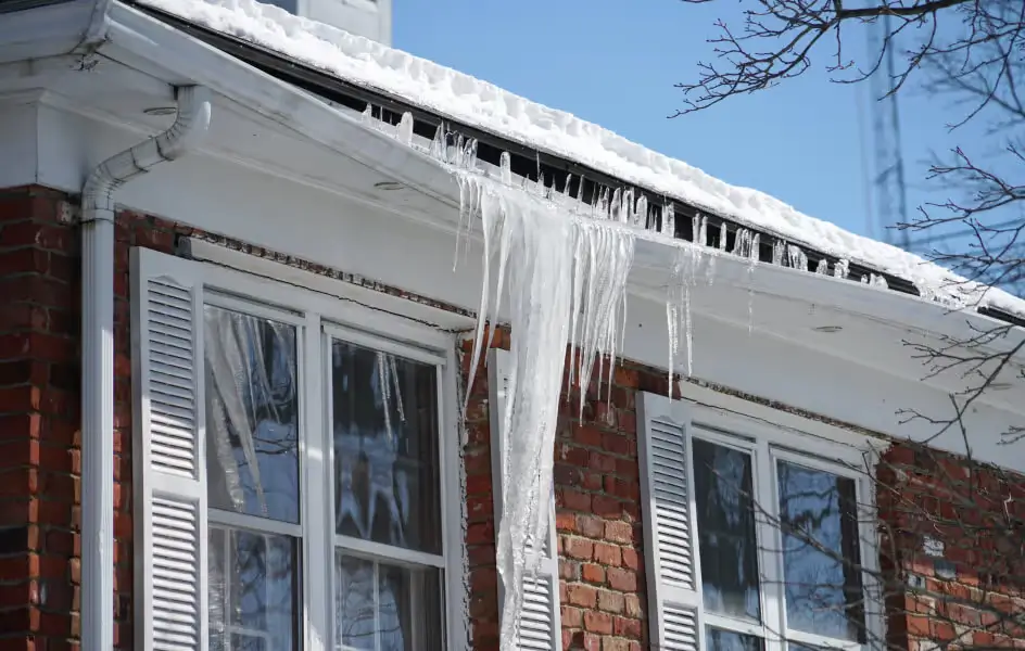 Large icicles hanging from a roof gutter on a brick home with snow buildup on the eaves