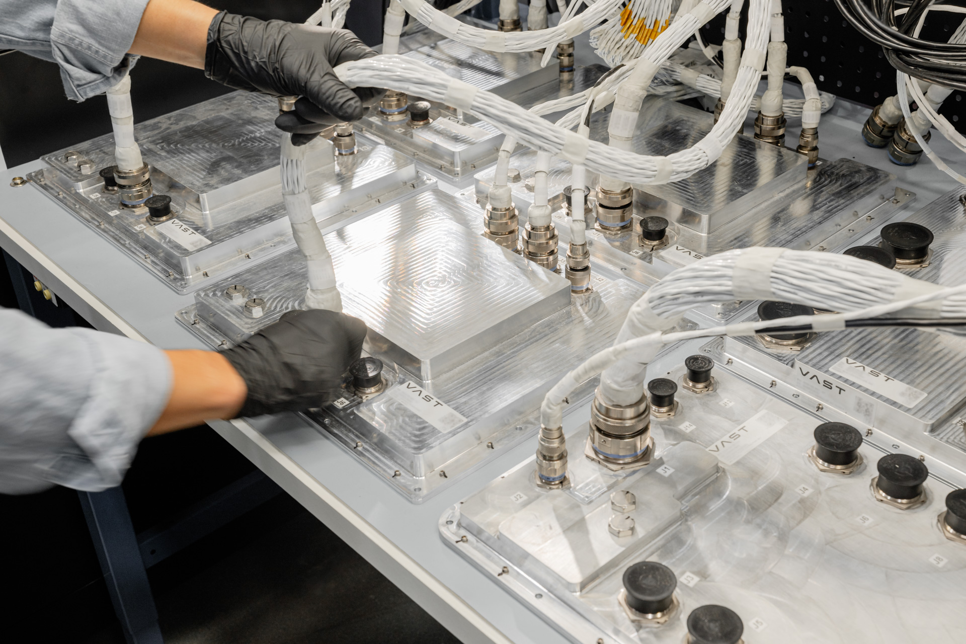 Black-gloved hands wire Vast CPUs configured for fault-tolerant power system testing on a worktable.