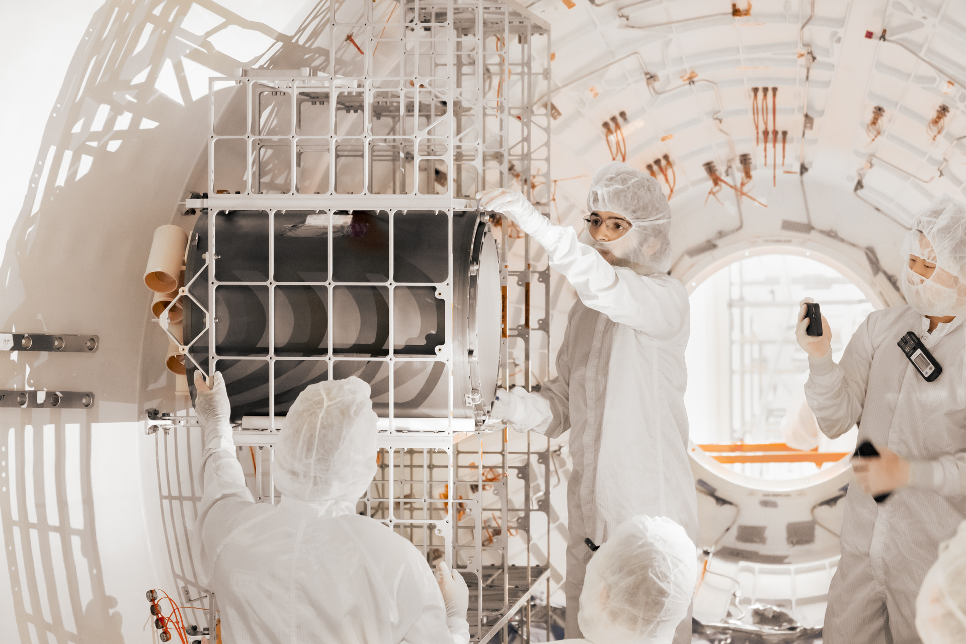 Four Vast employees in cleanroom gear work inside Haven-1, fitting a black cylinder into a chamber.