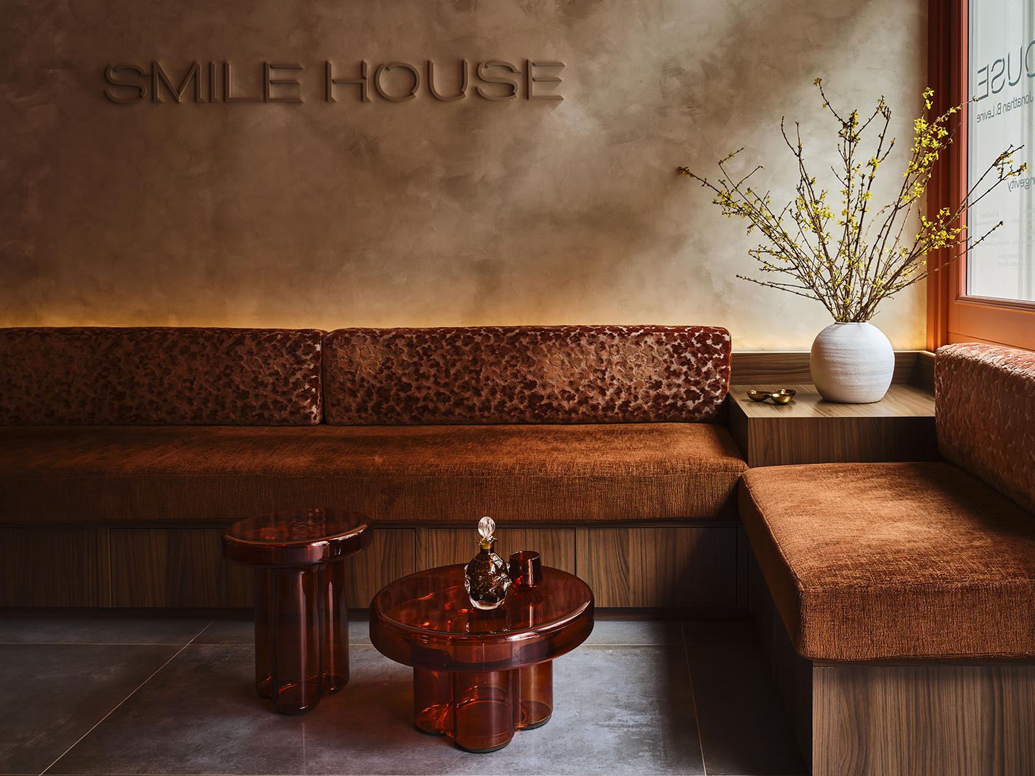 Smile House Tribeca reception with the SMILE HOUSE wordmark embossed in warm plaster above a rust velvet banquette