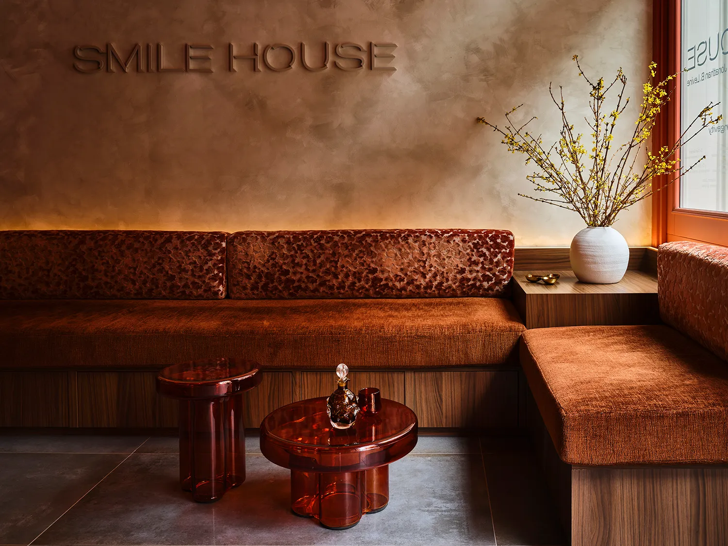 Smile House Tribeca reception with the SMILE HOUSE wordmark embossed in warm plaster above a rust velvet banquette