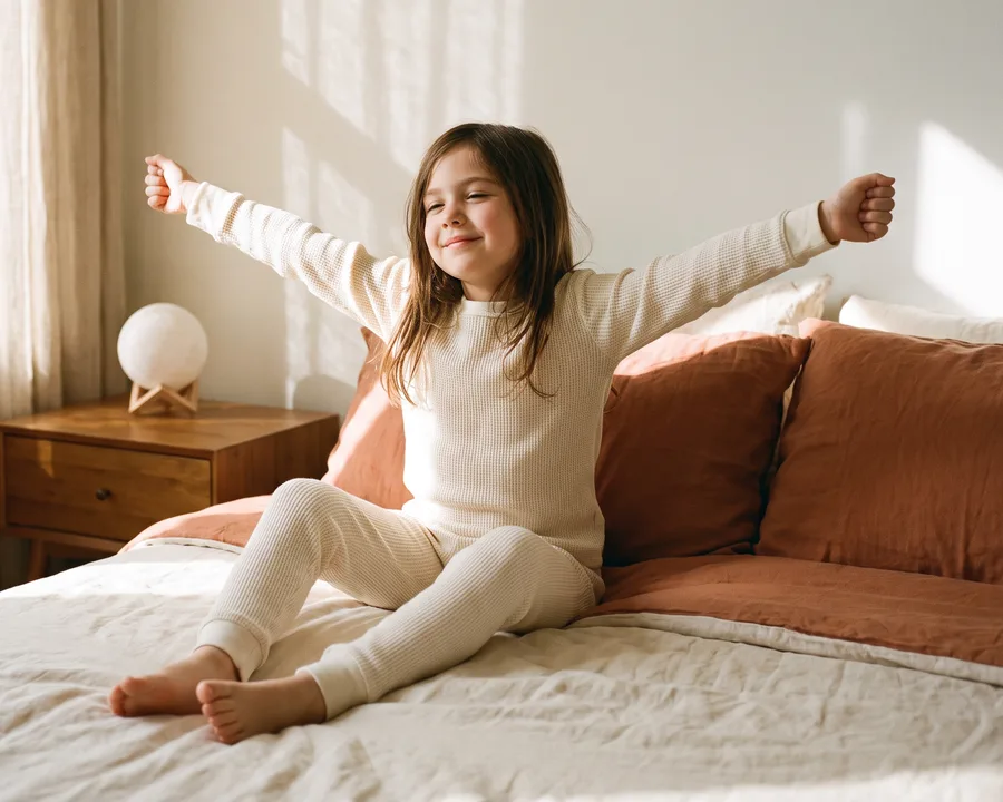 A rested girl stretching on her bed in morning sunlight