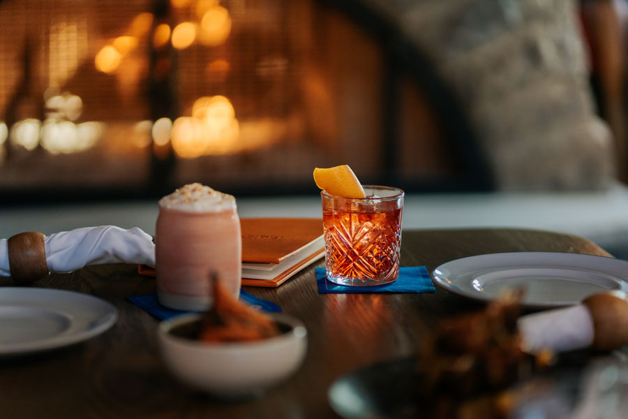 A negroni and Bluebird Colada sit on a fireside table. 