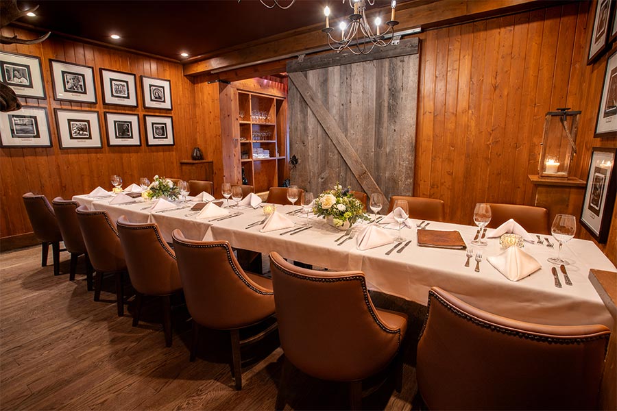 A long table for 14 is set with white linens and floral arrangements. The private room has a cozy, slightly rustic, wood panelled interior