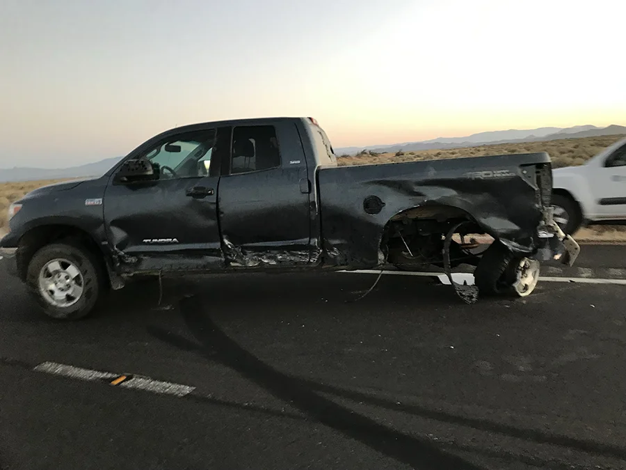 Damaged black pickup truck after a severe side-impact collision on a California highway, showing crushed doors and rear axle damage. Photo used for a truck accident case resulting in a $1.7 million settlement.