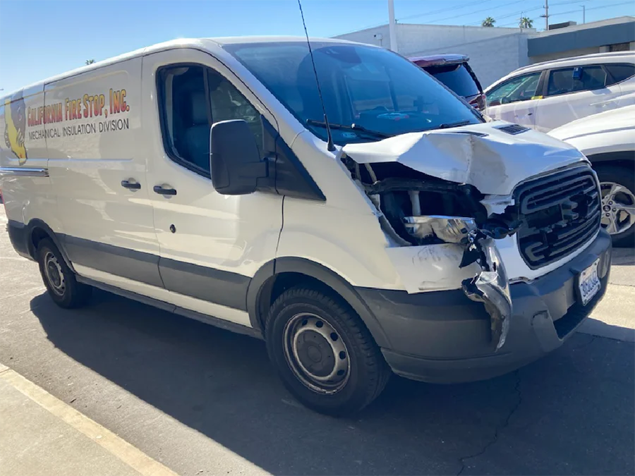 Daños en la parte delantera de una camioneta comercial de trabajo después de un accidente automovilístico en California, que muestran daños en el capó, los faros y el parachoques causados por una fusión de carriles insegura.