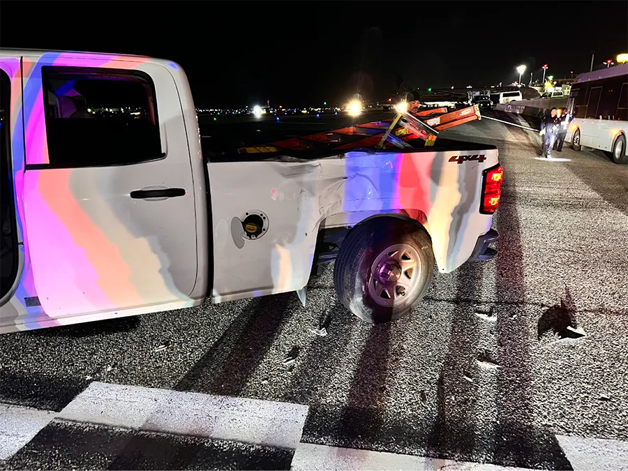 Side damage to a pickup truck after a shuttle bus collision at Los Angeles International Airport (LAX), showing impact to the truck bed and rear wheel under nighttime conditions.