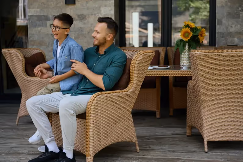 Father and son laughing while sitting on wicker lake house furniture