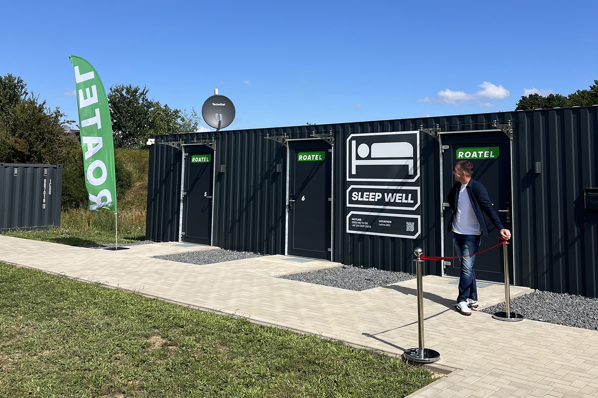 Vier Männer in Arbeitskleidung stehen vor einem großen orangefarbenen Container mit der Aufschrift Magnum und besprechen Unterlagen.