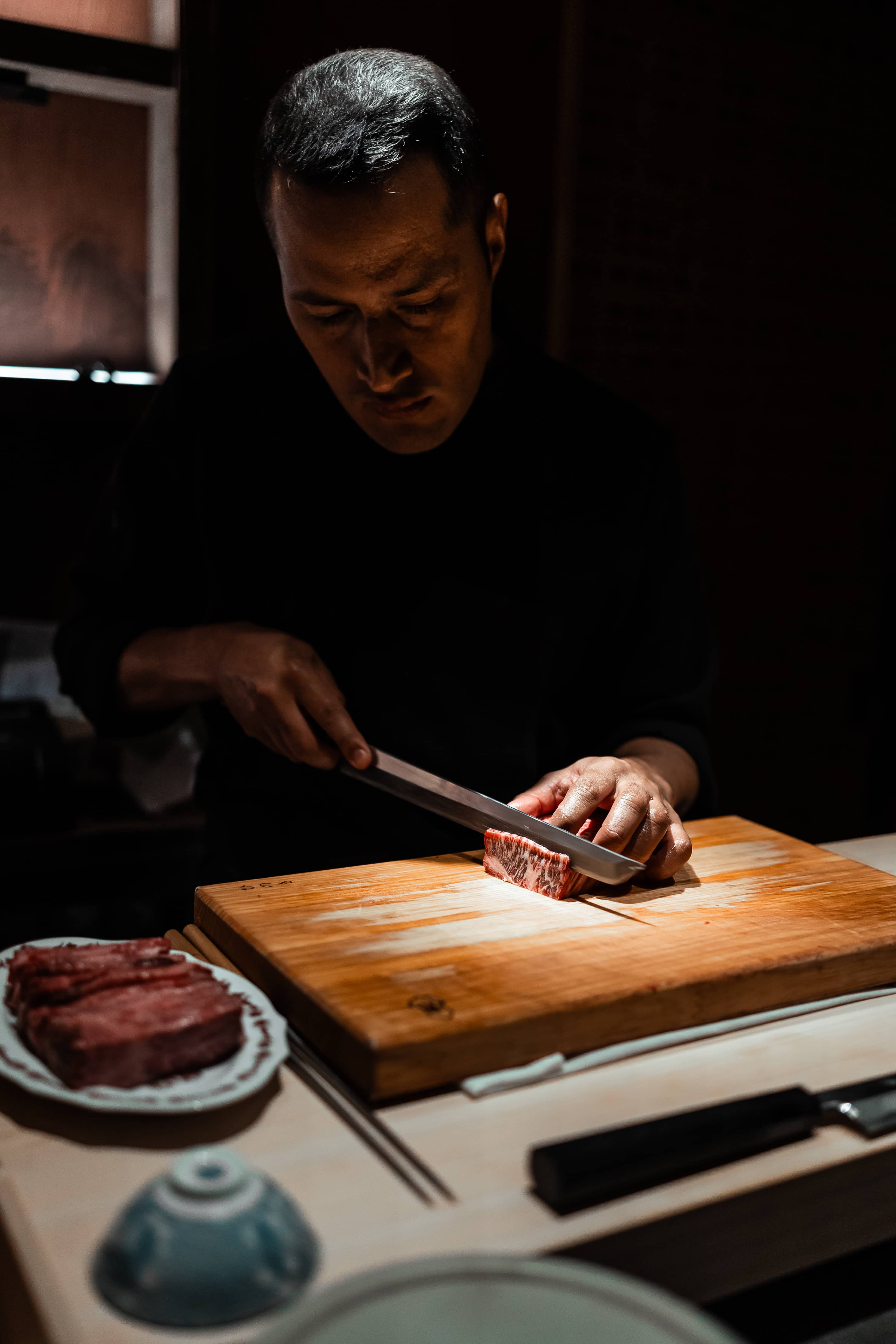 Chef découpant un morceau de thon rouge sur une planche en bois dans un restaurant gastronomique