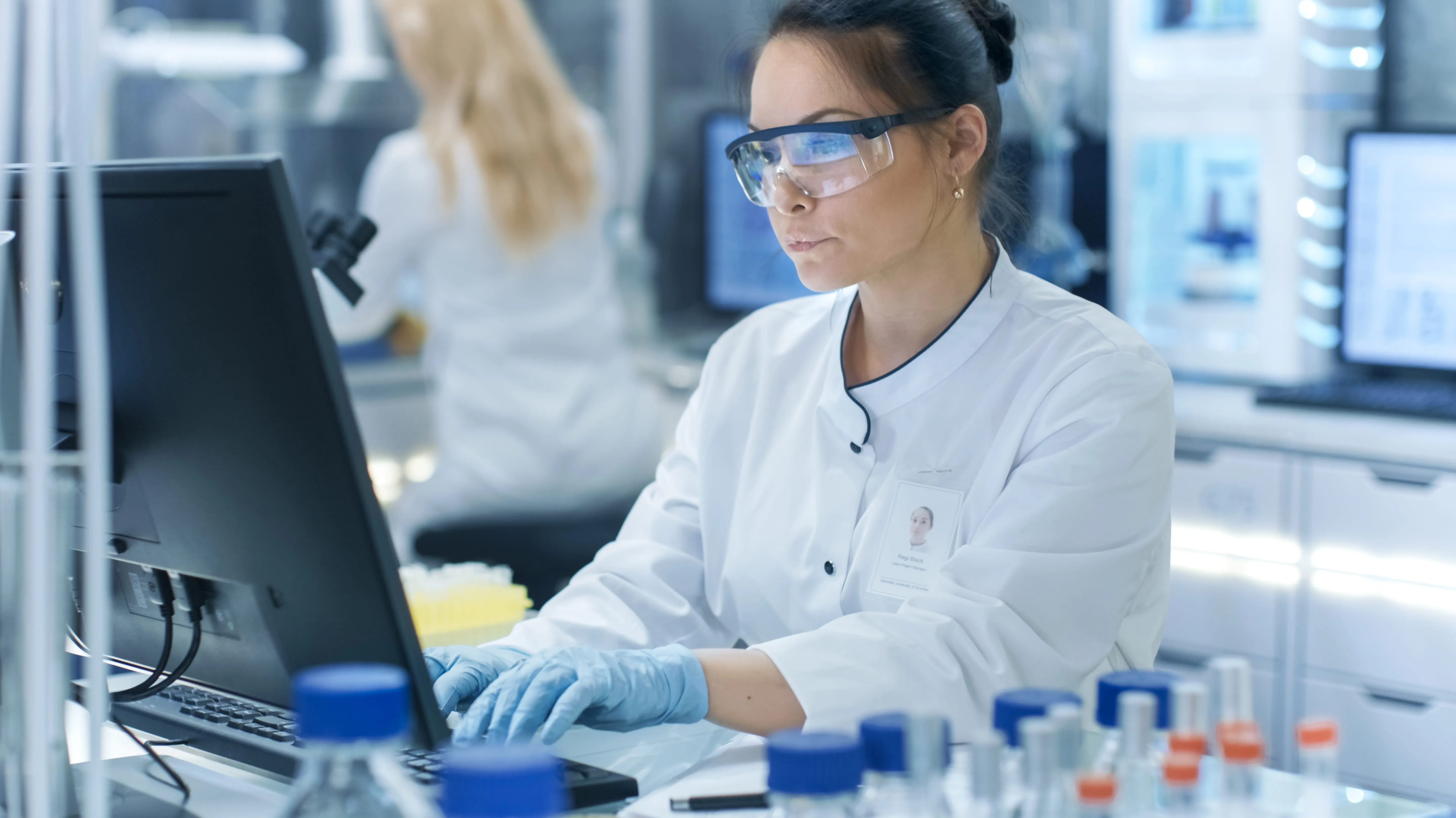 A female scientist wearing goggles is typing on a computer