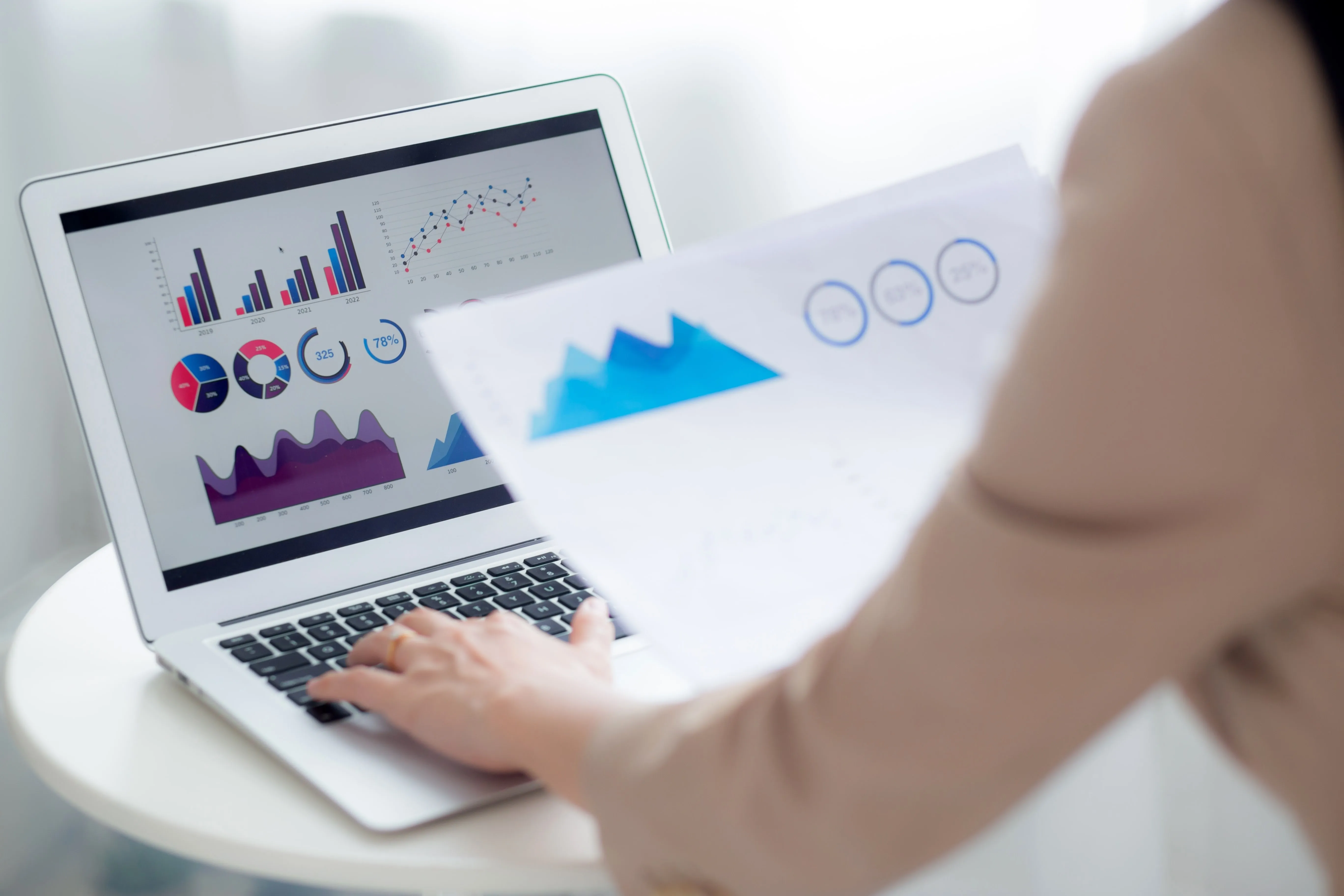A person is typing on a laptop with graphs on the screen