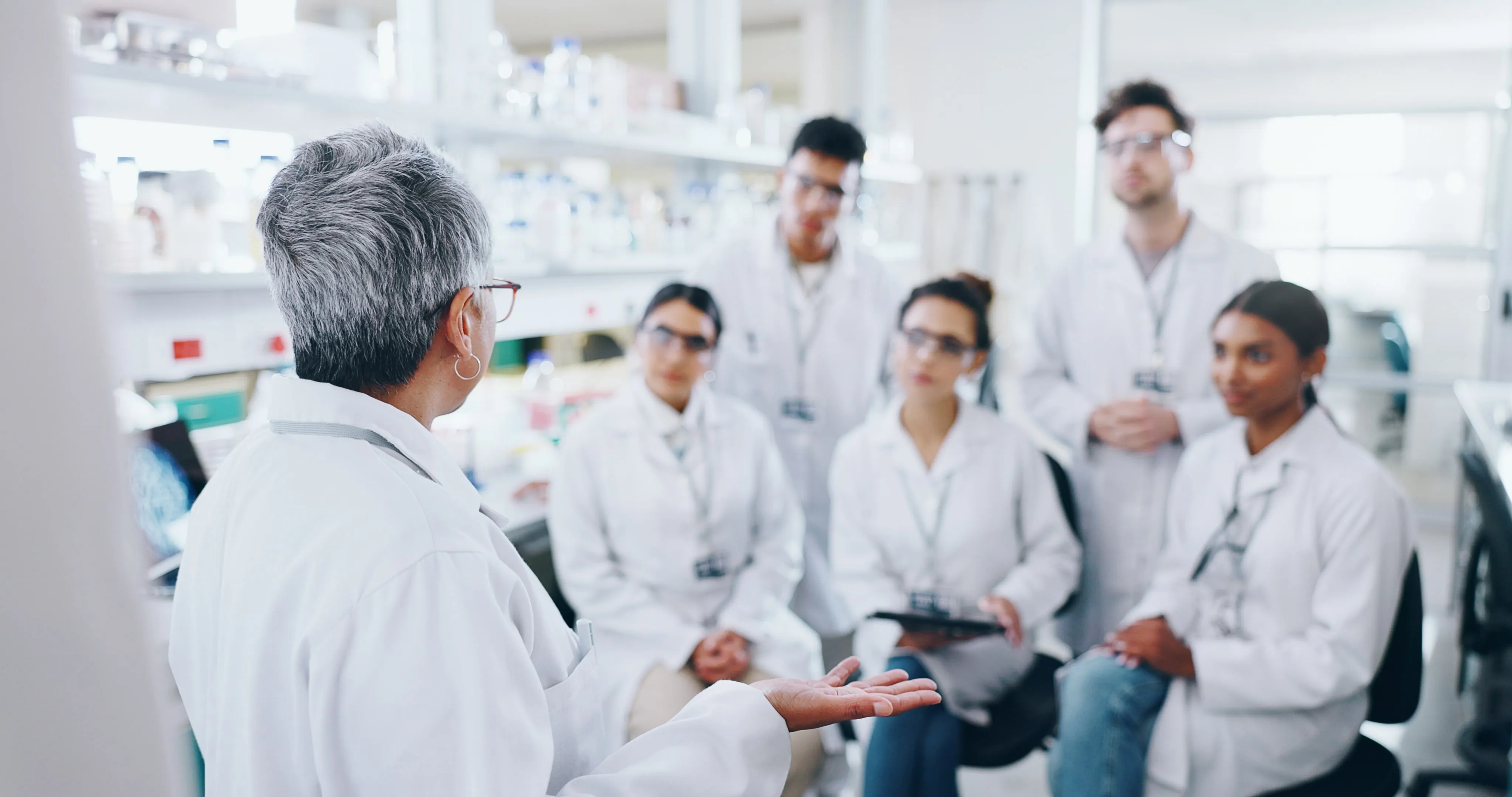 A group of scientists are gathered around a woman in a lab coat