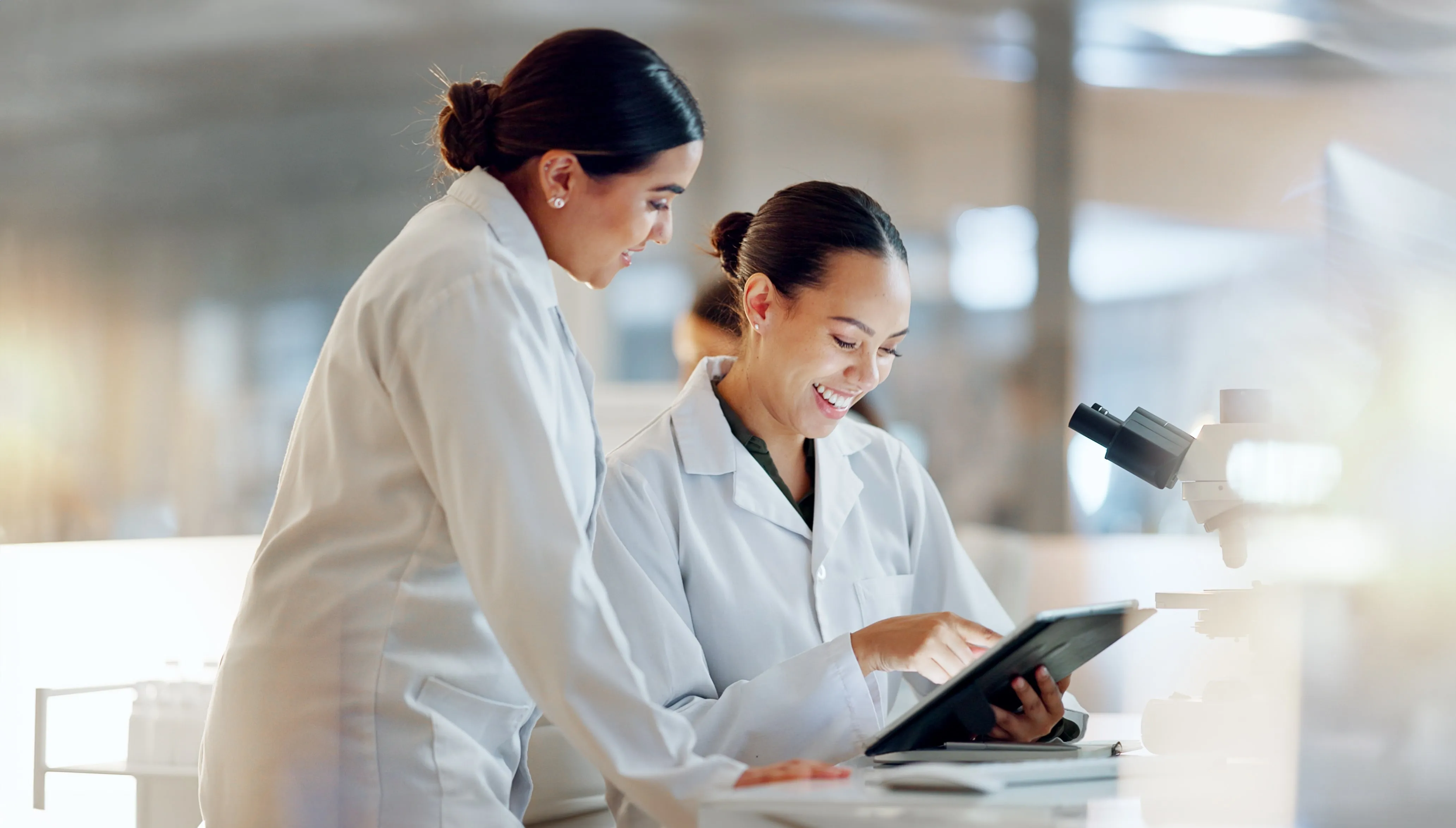 Two women in lab coats are looking at a tablet
