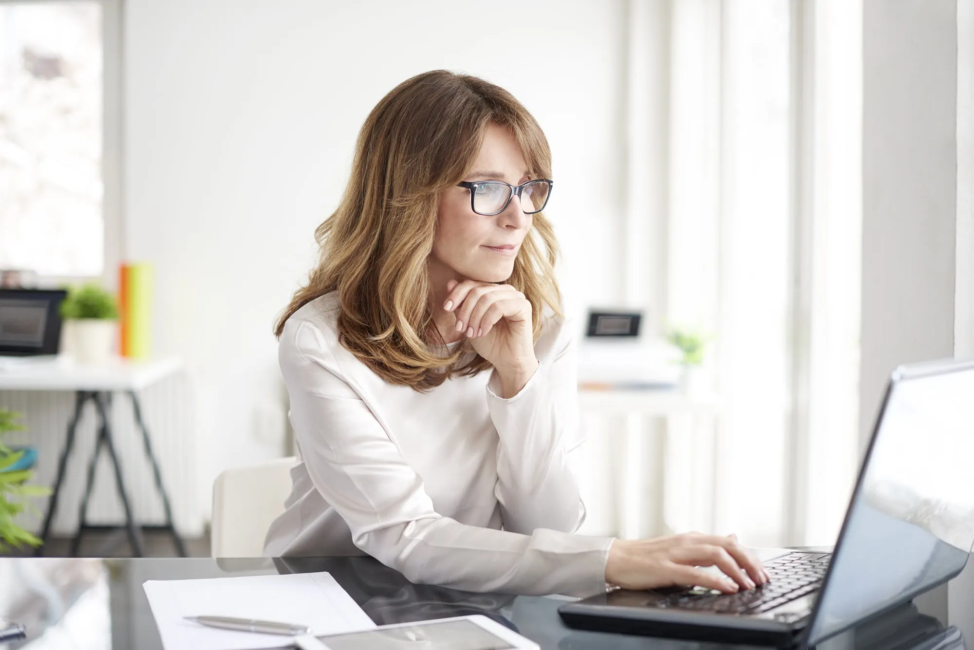 A woman wearing glasses is typing on a laptop