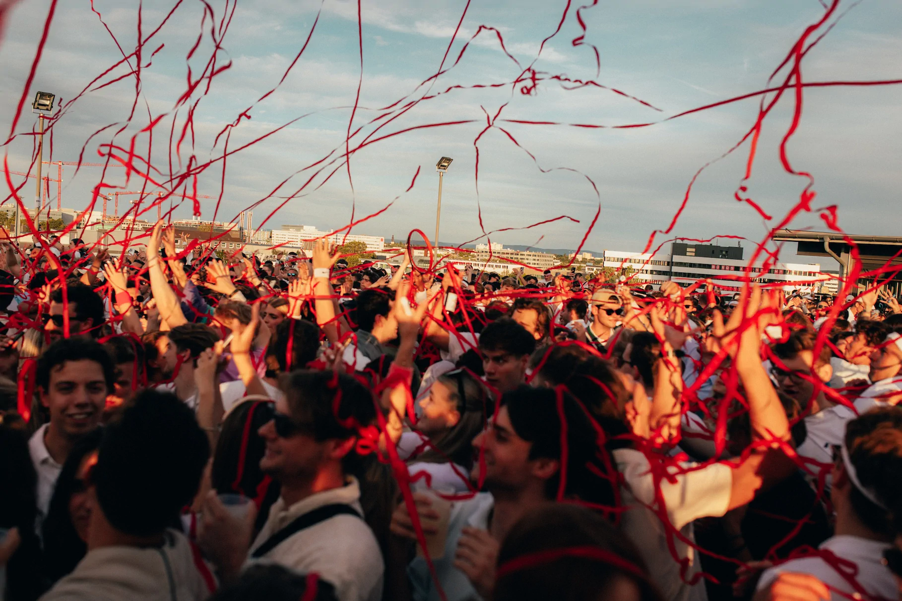 Menschenmenge bei einer Feier im Freien mit roten Luftschlangen in der Luft unter blauem Himmel.