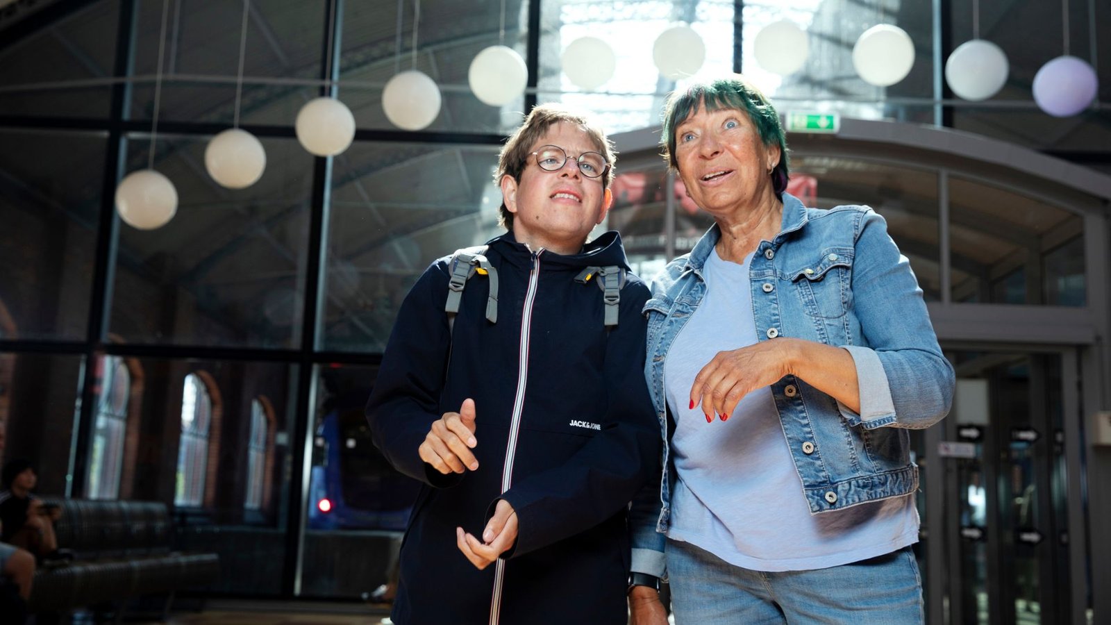 Två personer arm i arm i en ljus hall med lyktor, skrattande