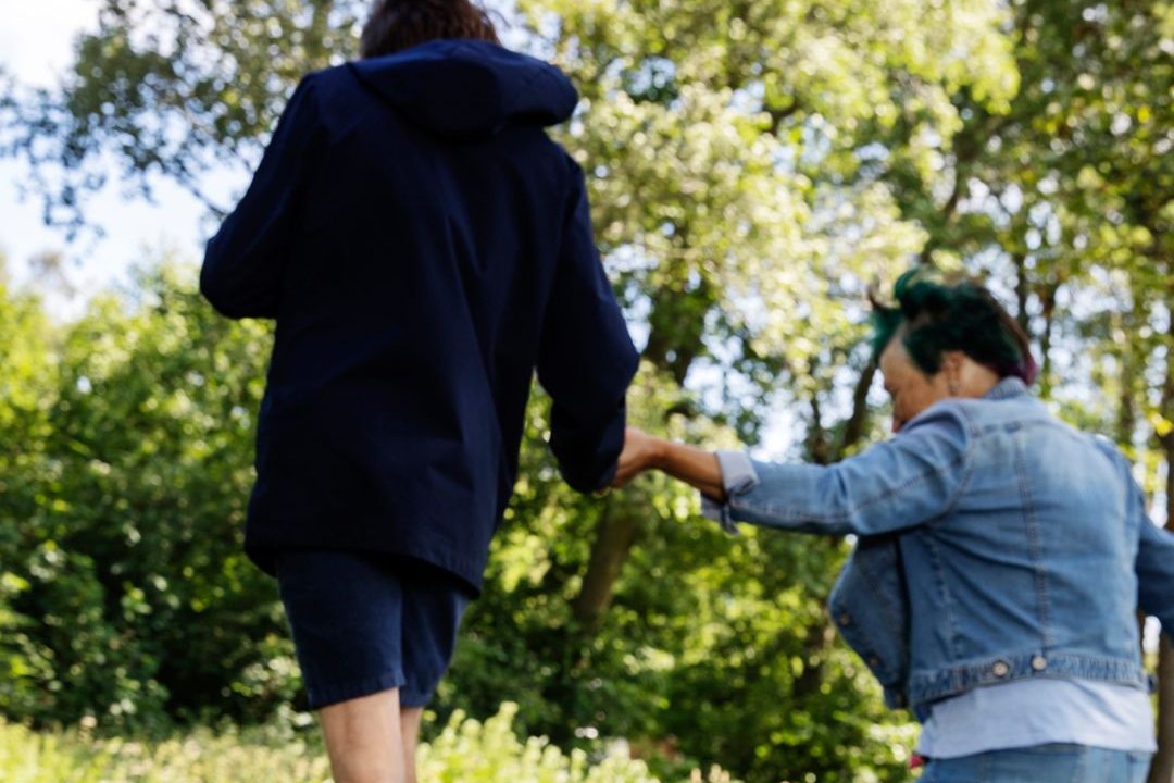 Person balanserar på en stock i skogen med stöd av en assistent