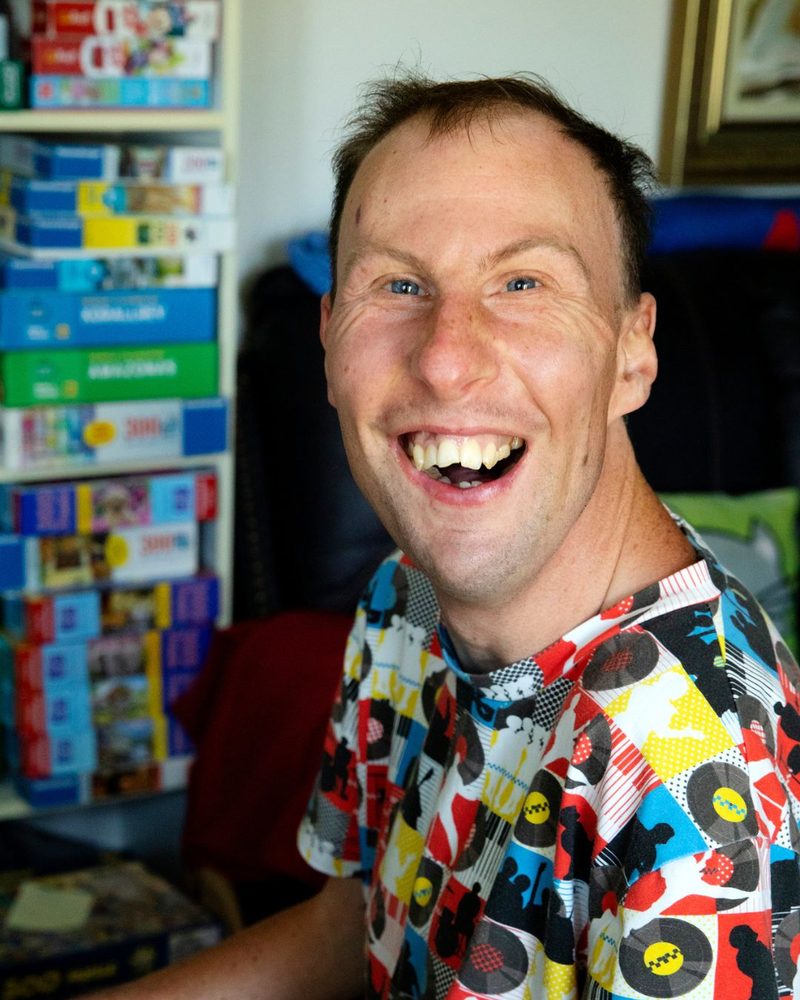 Man i färgglad skjorta skrattar i sitt vardagsrum