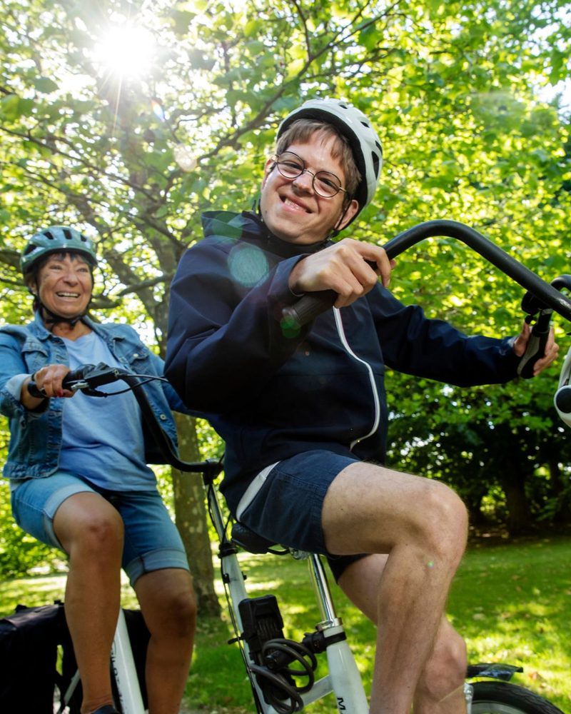 Ung man med hjälm på trehjuling i parken, sedd uppifrån