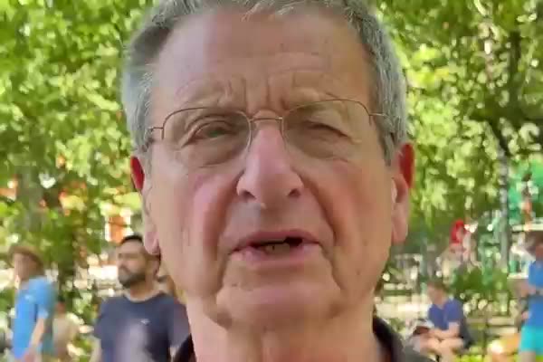 A still from a Happy Productions video: a man speaking outdoors at a community event