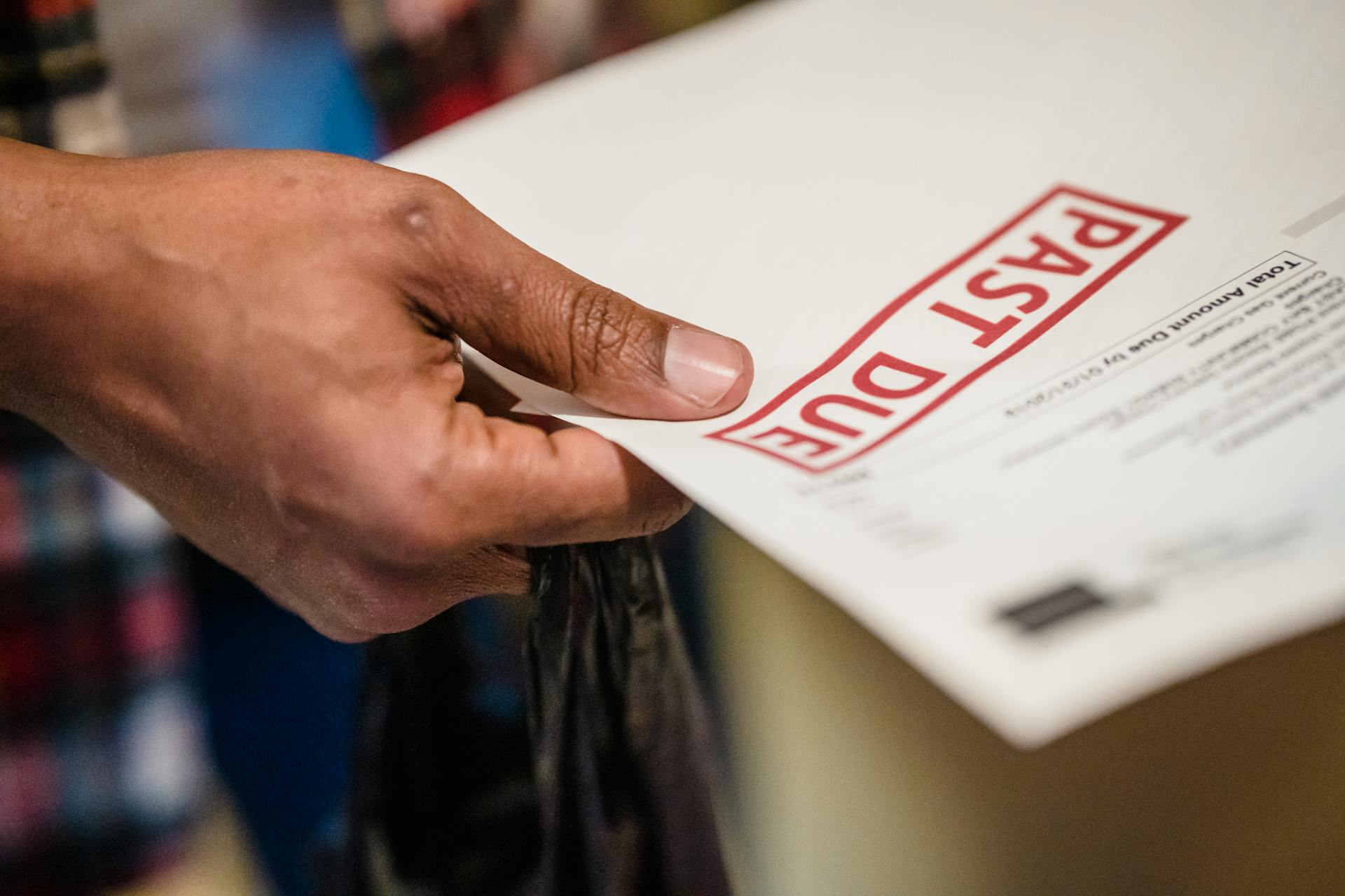 Close-up of a hand holding an envelope or document stamped with a red “PAST DUE” label
